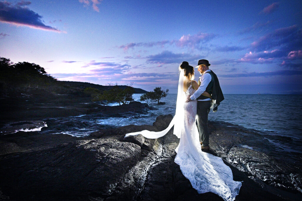 A bride and groom hung on beach rocks at night with flash photography at Villa Botanica.