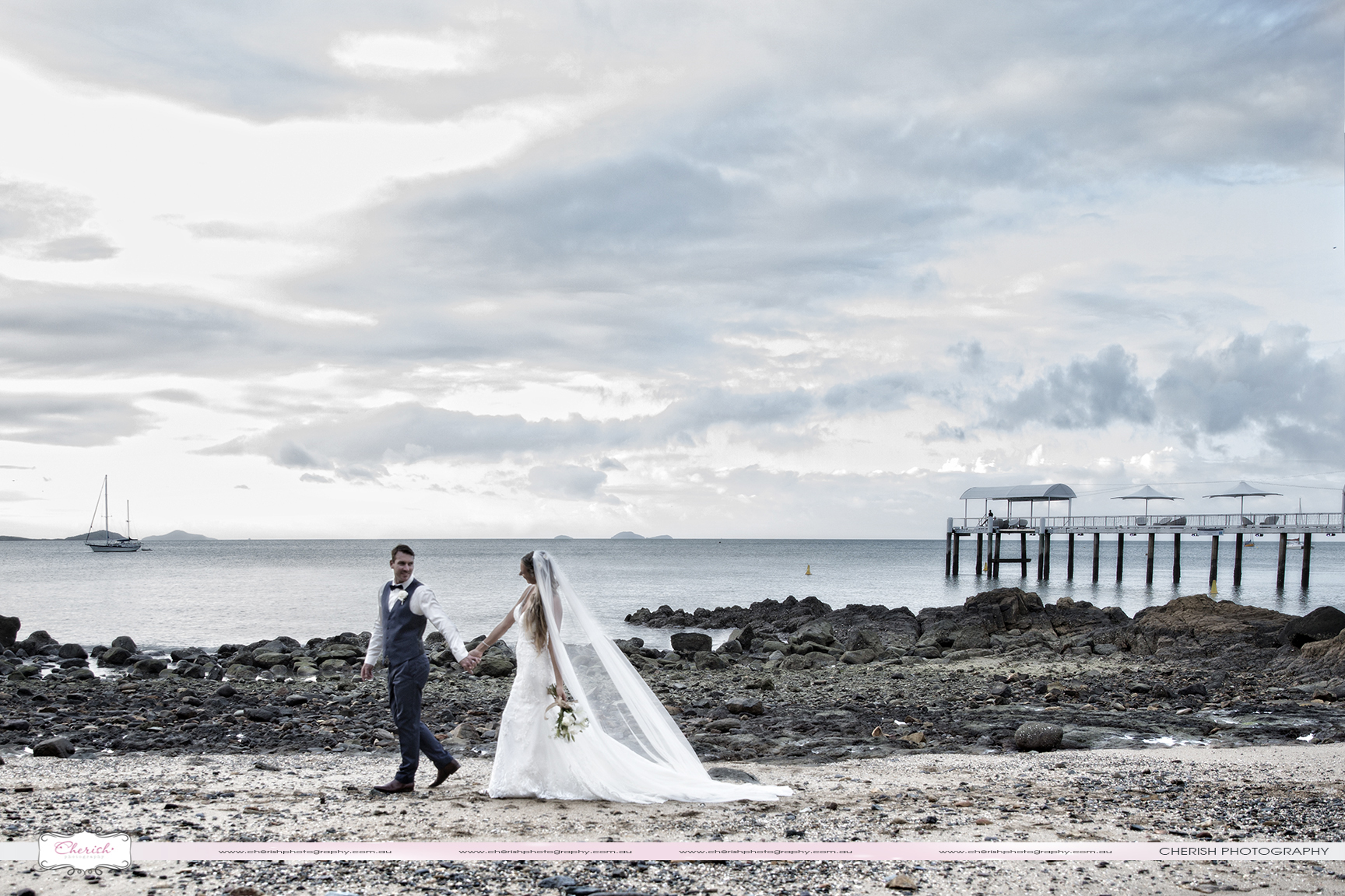 A bride and groom walking on the beach near the Coral Sea Resort in Airlie Beach QLD - artistic wedding photography.
